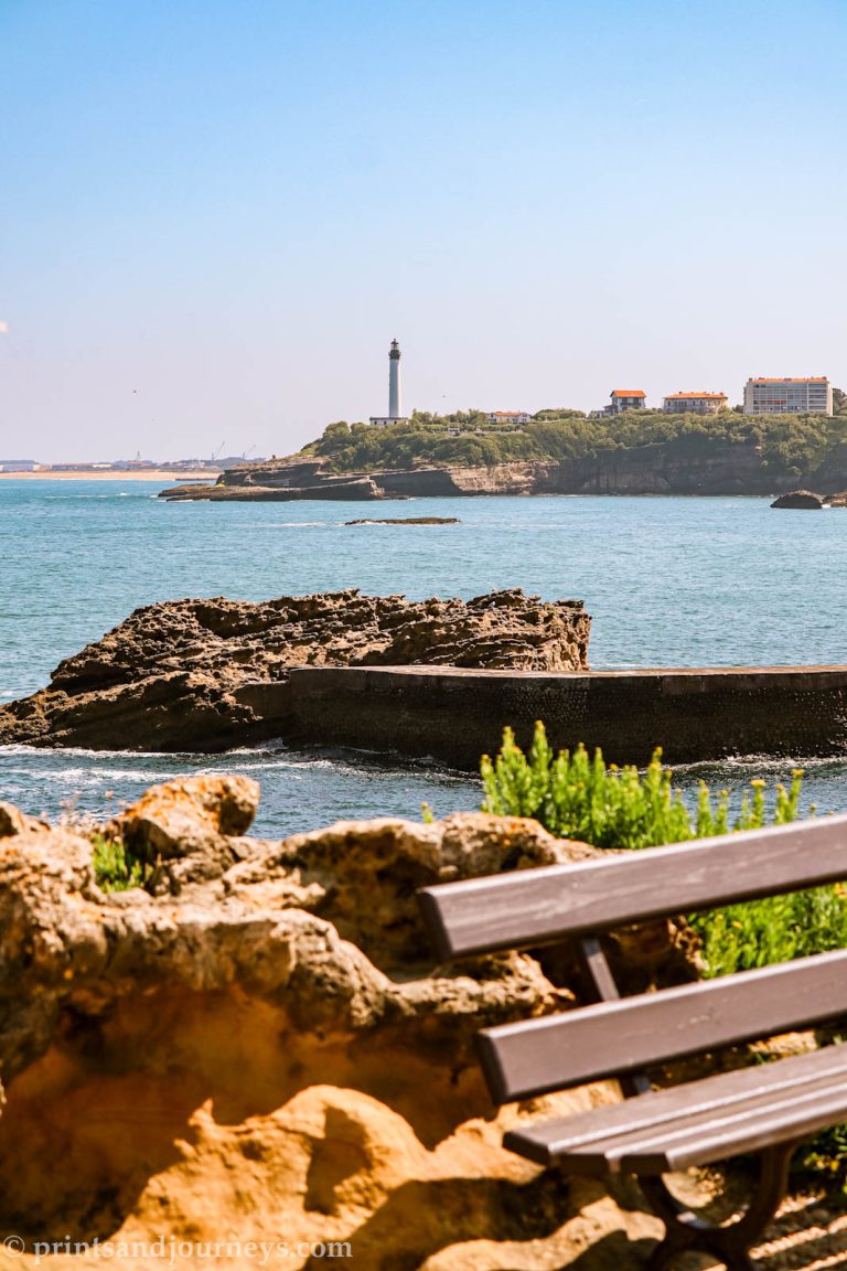 View of the biarritz lighthouse in the background with rock and a bench sitting in the foreground
