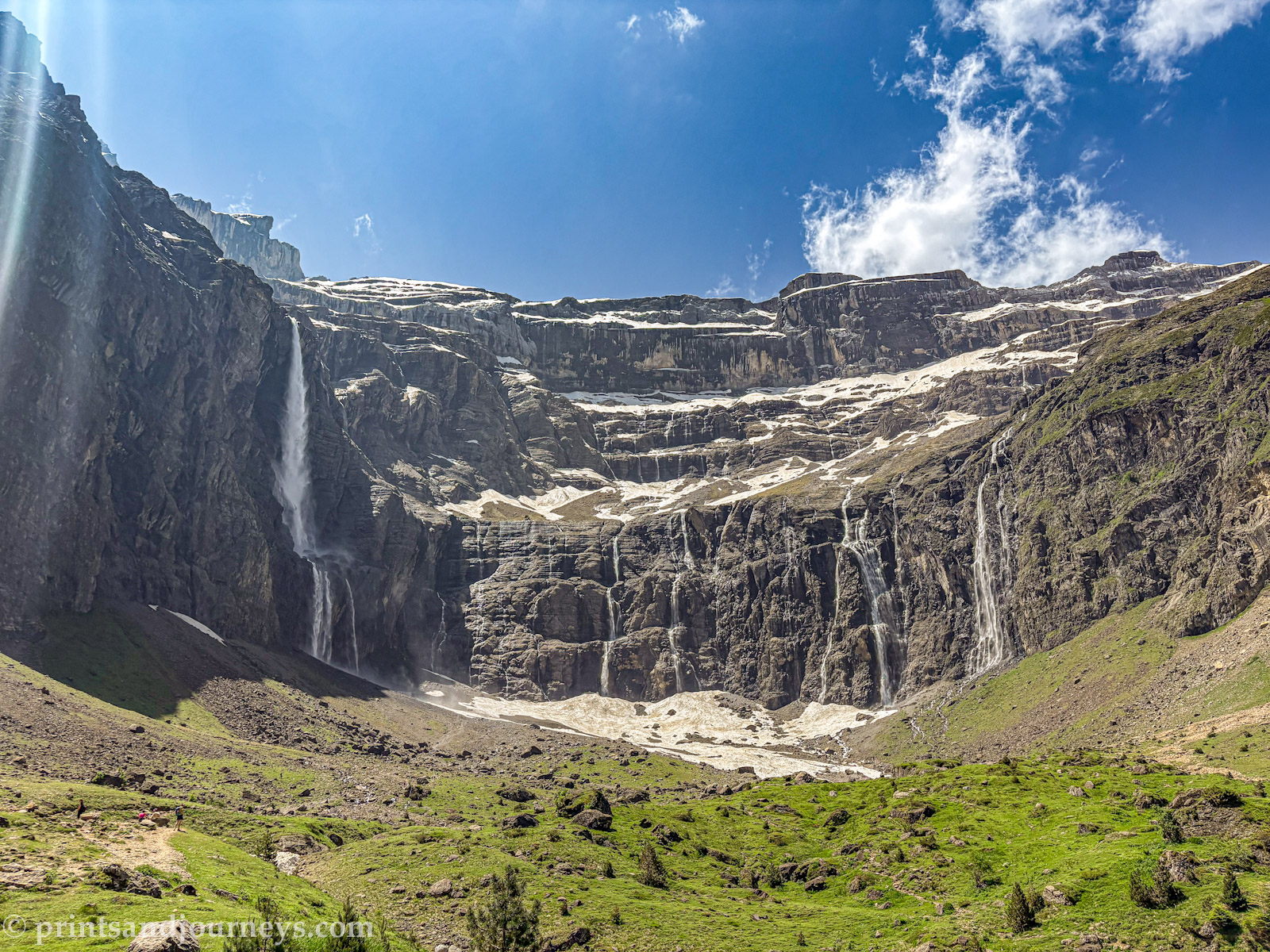 Panoramic view of Cirque de Gavarnie in the French Pyrenees, showing multiple cascading waterfalls flowing from the amphitheatre-shaped cliffs surrounded by rugged mountain peaks.