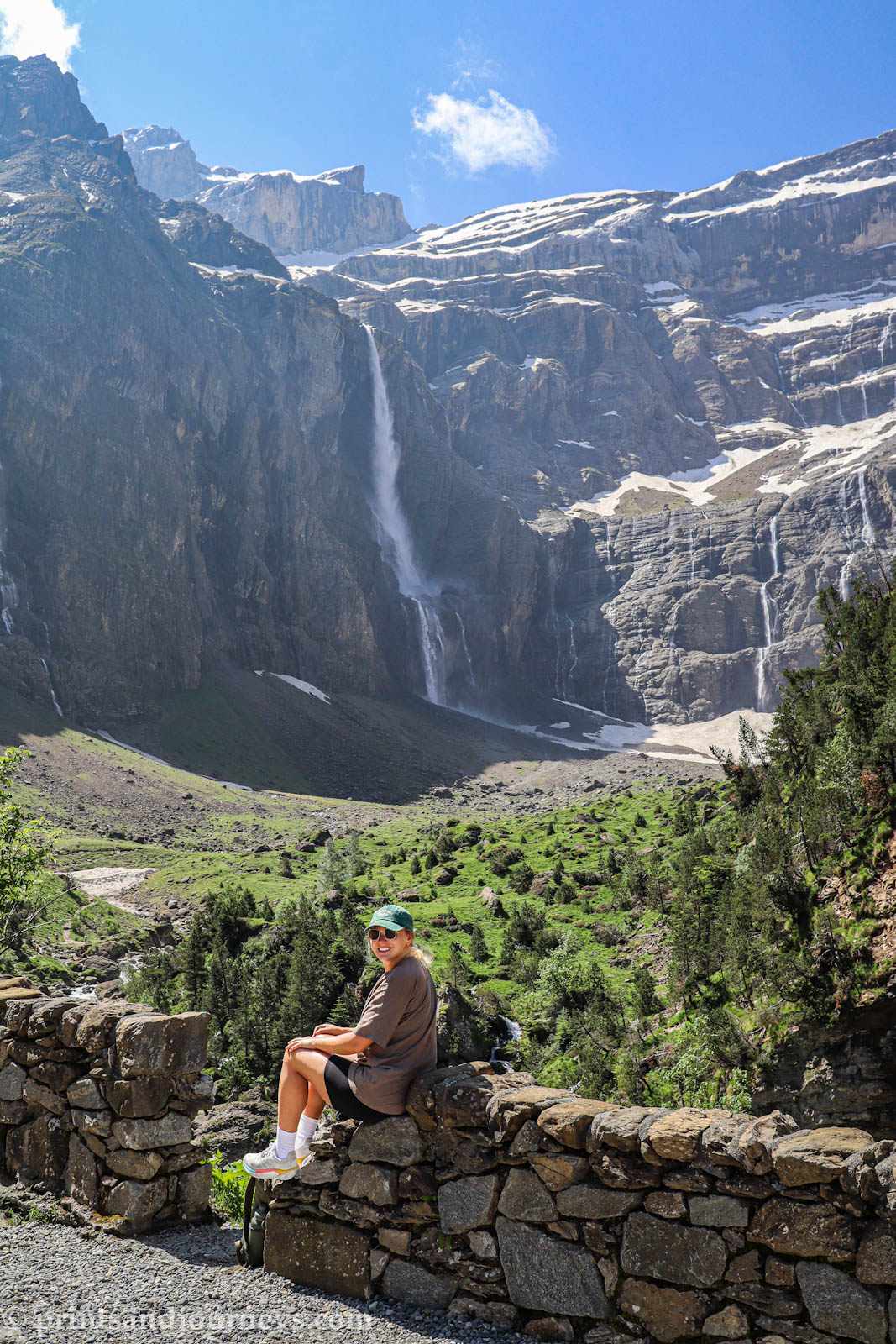 Girl sitting on a small rock wall with the Grande Cascade de Gavarnie and towering cliffs of the Cirque de Gavarnie in the French Pyrenees in the background