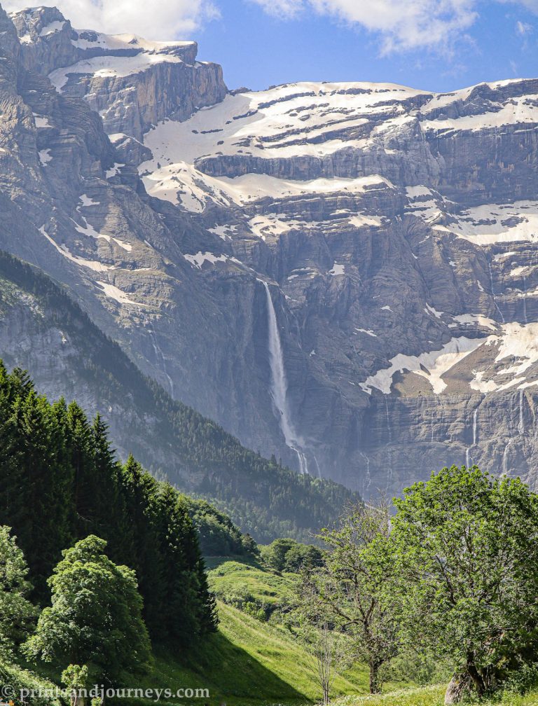 Cirque de Gavarnie in the French Pyrenees, featuring the main waterfall front and center with massive cliffs rising behind, framed by grass and trees in the foreground.