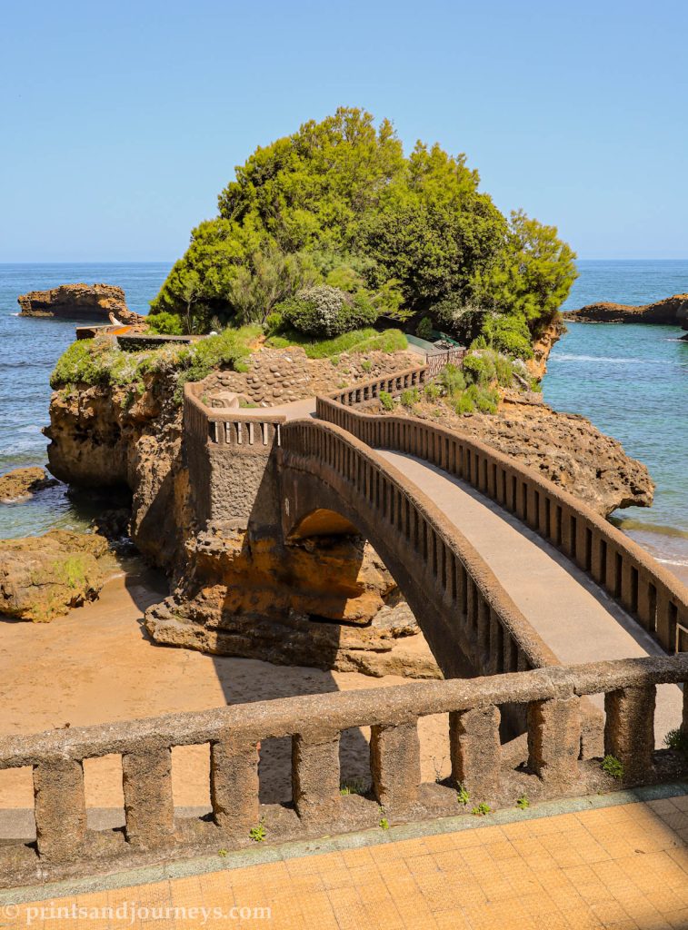 Basta Rock rising from the ocean near the beach, connected by a graceful arching bridge.