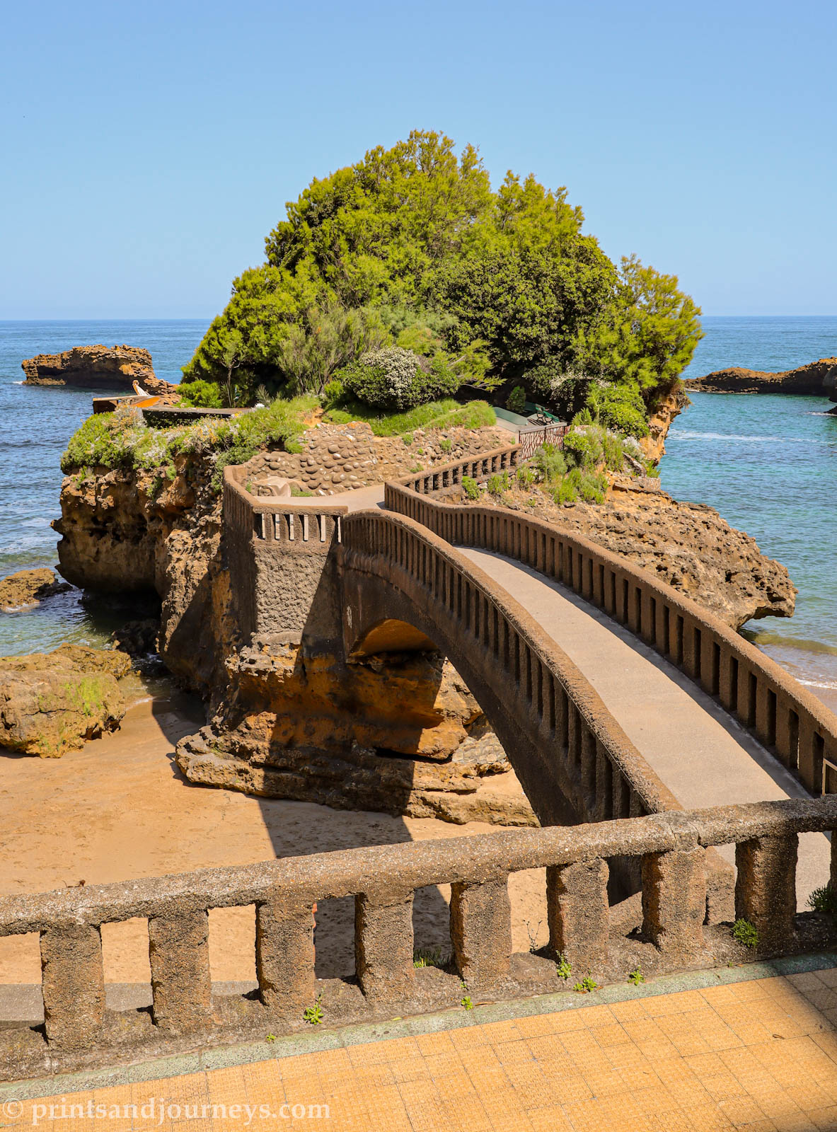 Basta Rock rising from the ocean near the beach, connected by a graceful arching bridge.