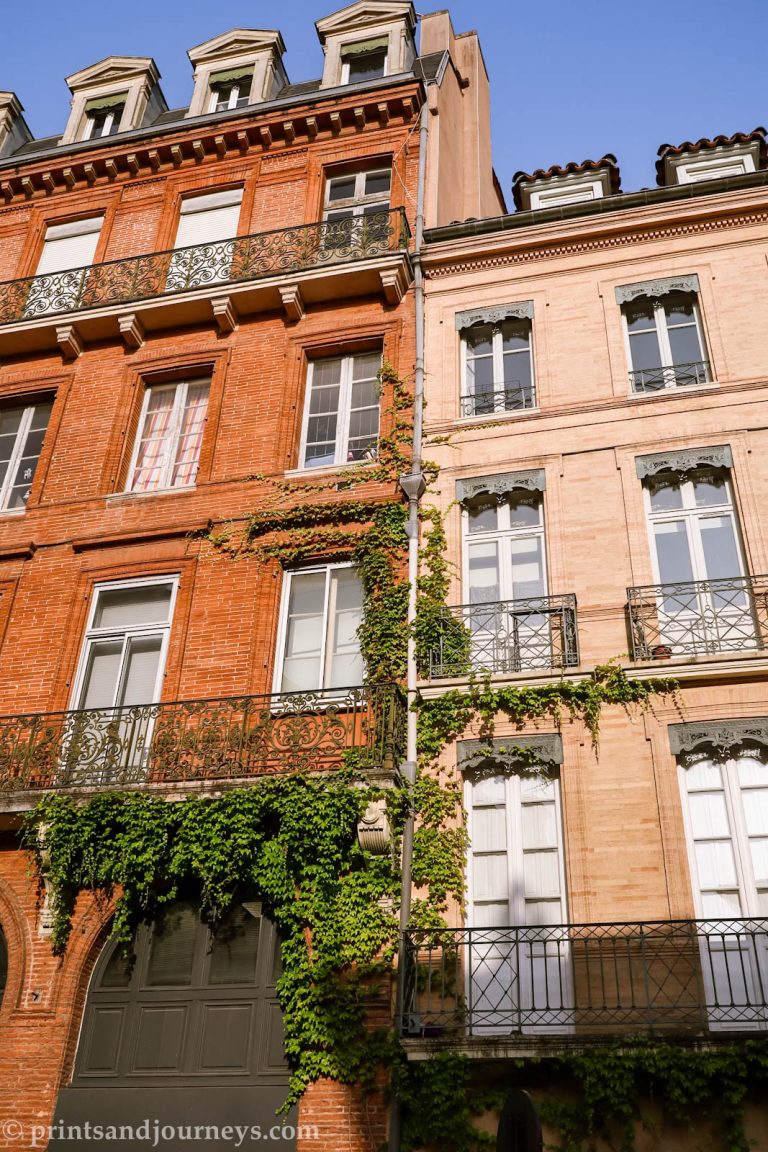 red brick and pink terracotta apartments with vines growing up them against a blue sky in Toulouse France