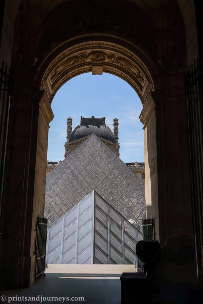 The louvre glass pyramids in frame with an archway
