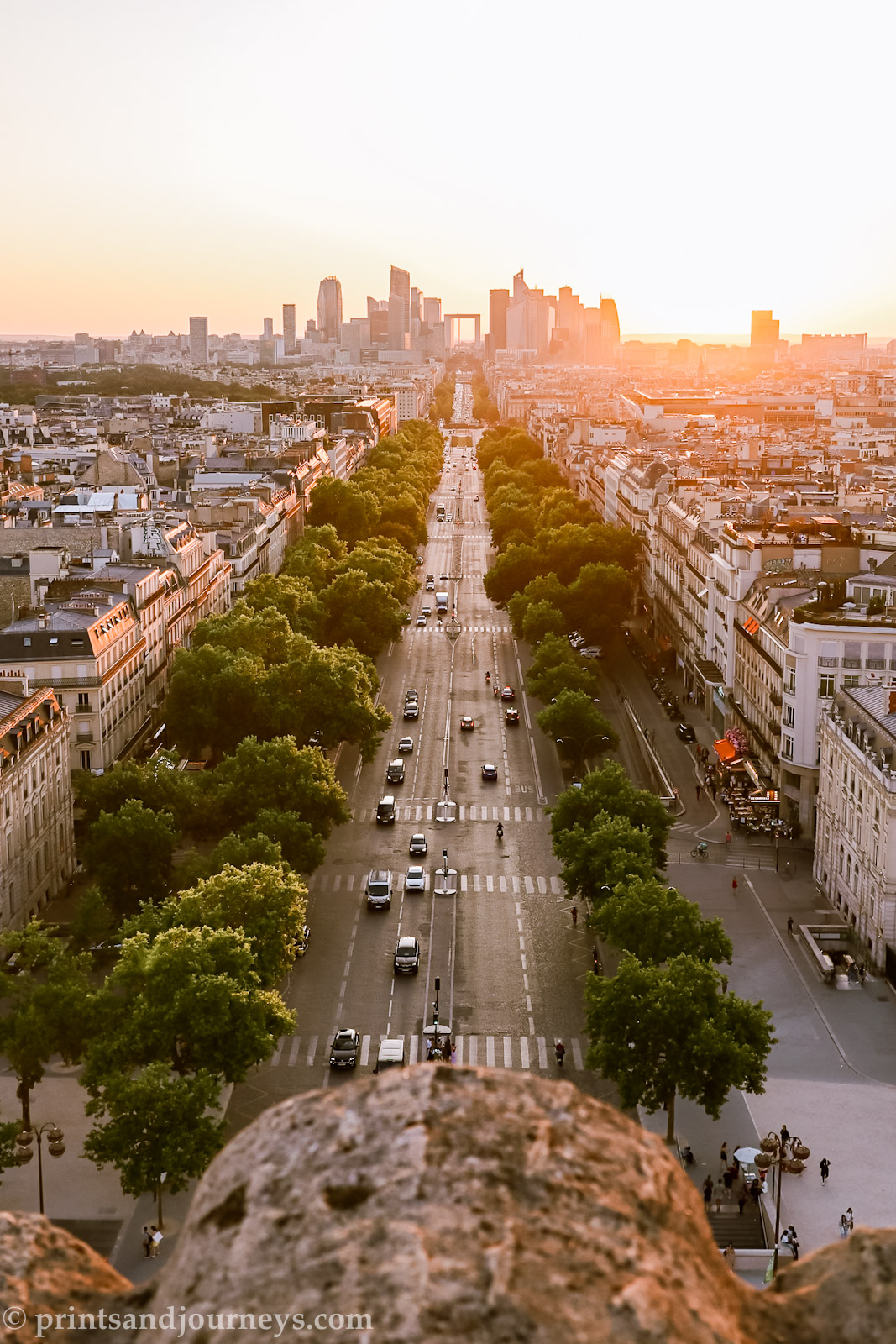 Sunset view down the main avenue from the Arc de Triomphe, with the iconic grande arche glowing at the end of the street in Paris