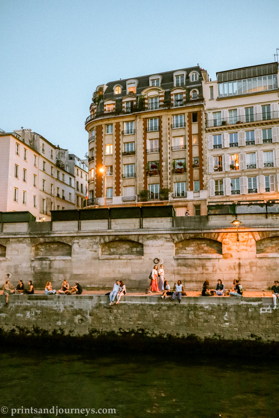 the banks of the seine in the summer at dusk with people lounging along the edge