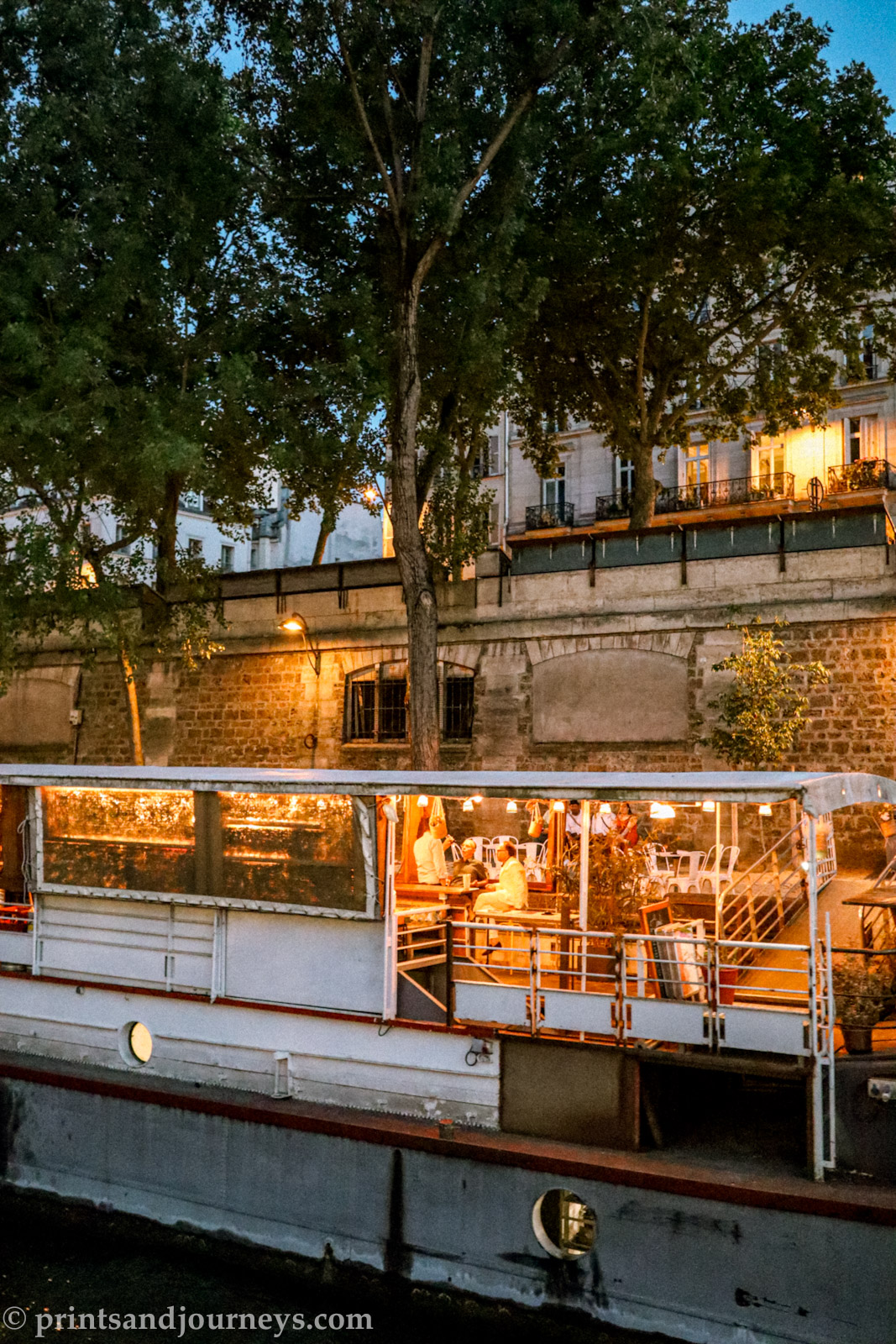 a cozy bar in a boat parked along the banks of the seine in Paris with trees behind it